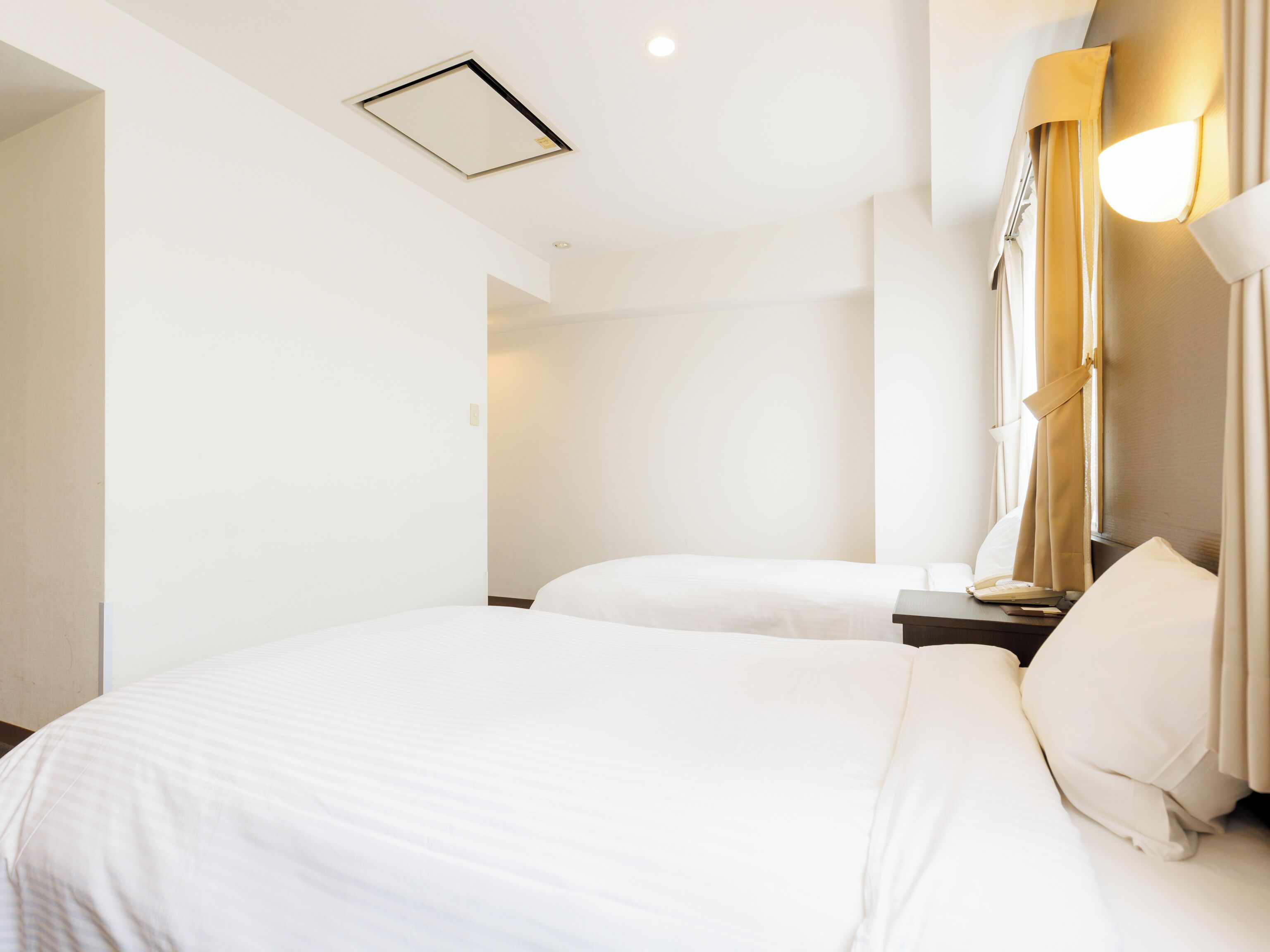 A hotel room with two beds, a bedside table, a lamp, and a ceiling light.