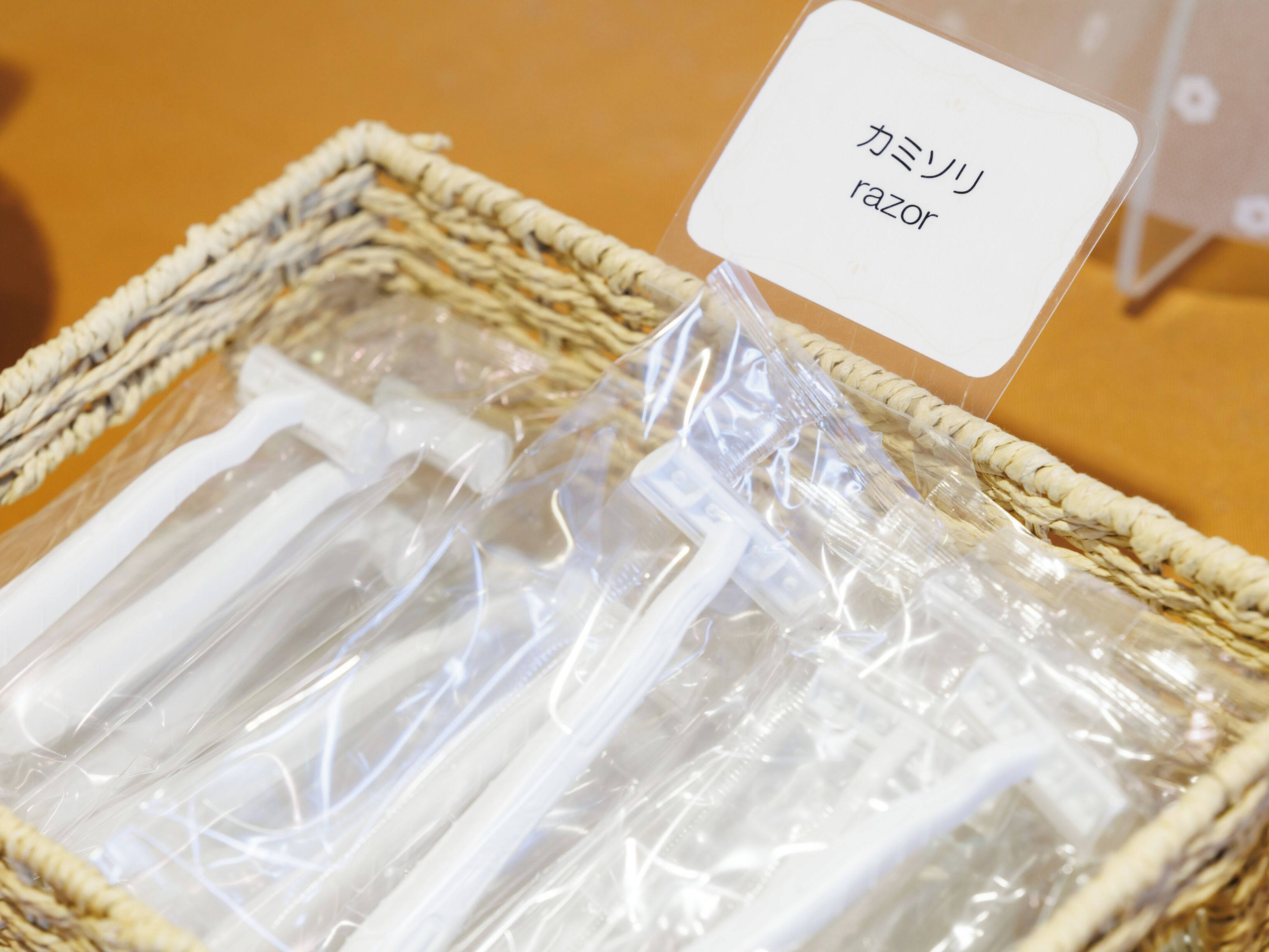 A wicker basket containing several clear plastic bags with white items, possibly razors, and a label with Japanese text.
