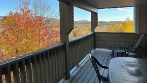 Un espace extérieur abrité, offrant une vue sur le feuillage automnal, avec une terrasse en bois et une table entourée de chaises.