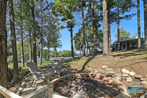Eine Blockhütte am See mit Feuerstelle, zwei Adirondack-Stühlen und Seeblick.
