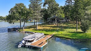 A lakeside property with a dock, a covered boat, and a house surrounded by trees.