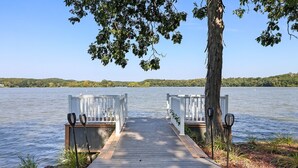 A wooden dock leading to two white paddle boats on a lake with a forested hill in the background.