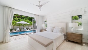 Een moderne slaapkamer met een groot bed, een nachtkastje, een plafondventilator en uitzicht op een zwembad en groen buiten.
