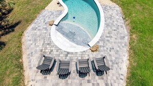 An aerial view of a swimming pool with a curved edge, surrounded by a paved deck with lounge chairs. - OFF THE GRID-Custom Showplace w/ Private Pool;Multiple Decks;3 Minute Walk to Beach (Edisto Beach)