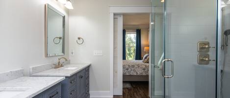 A bathroom with a glass shower enclosure, a double sink vanity, and a large mirror.