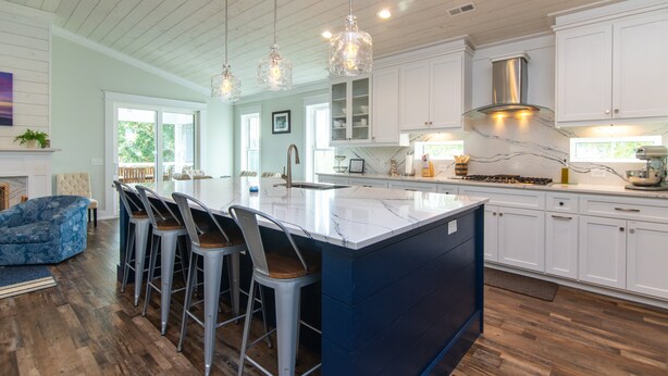A modern kitchen with white cabinets, a large island with bar stools, pendant lighting, and a view to the outdoors. - OFF THE GRID-Custom Showplace w/ Private Pool;Multiple Decks;3 Minute Walk to Beach (Edisto Beach)