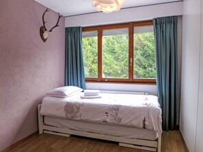 Een slaapkamer met een bed, een raam met gordijnen, een aan de muur bevestigd decoratie van een hertenhoofd en een plafondlamp.