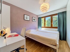 A bedroom with a bed, a desk, a chair, a lamp, and a window with curtains.