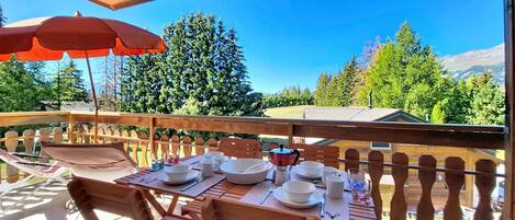 A wooden deck with a table set for dining, overlooking a forested area with mountains in the distance.