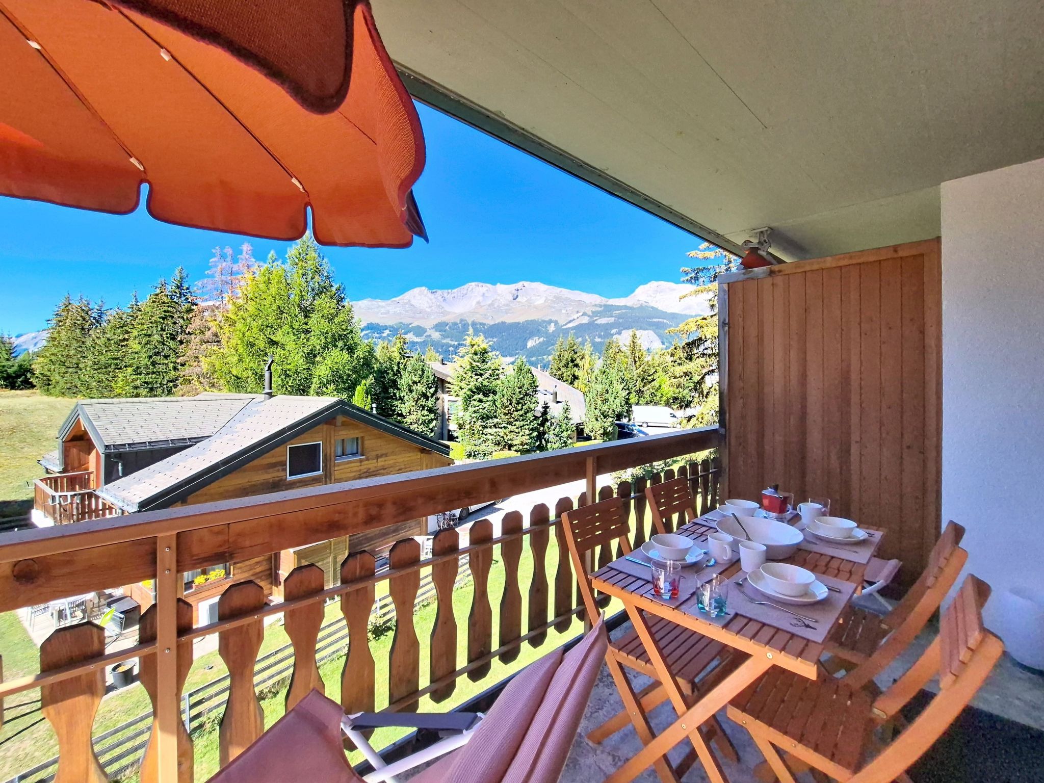 A balcony with a view of a mountain, wooden furniture, and a table set for dining.