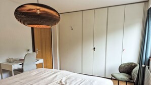 Un dormitorio con cama, escritorio, silla, armario y lámpara colgante.