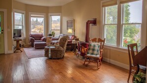 A spacious living room with hardwood floors, a ceiling fan, large windows, a fireplace, and a variety of seating options including a leather couch, armchairs, and a rocking chair. - Historical Victorian with Modern Touch. Garage with EV Charger (Sonora)