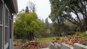 A residential backyard with a stone retaining wall, a tree, and a grassy area. - Historical Victorian with Modern Touch. Garage with EV Charger (Sonora)