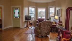 A living room with a television, a fireplace, and a view of a cityscape through large windows. - Historical Victorian with Modern Touch. Garage with EV Charger (Sonora)
