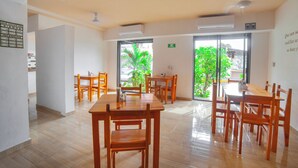 A spacious dining area with wooden tables and chairs, large windows with a view of greenery, and an air conditioning unit on the ceiling. - Hotel del profe (Santa María Huatulco)