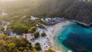 An aerial view of a beach with a parking area, beach umbrellas, and a small building with a sign. - Hotel del profe (Santa María Huatulco)