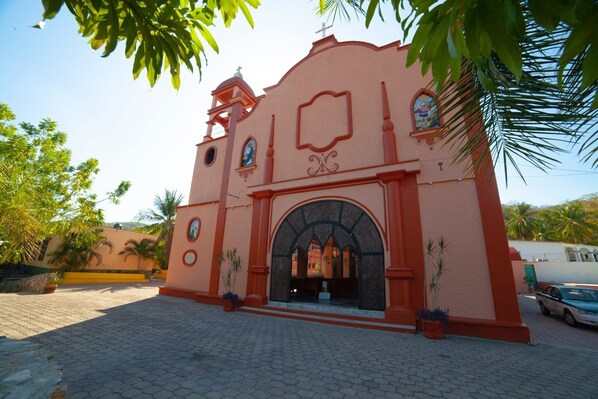 A church with a red facade, a bell tower, and an arched entrance. - Hotel del profe (Santa María Huatulco)
