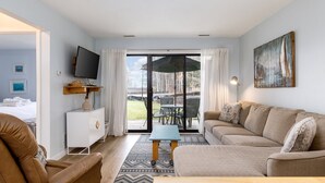 Een moderne woonkamer met een bank, een salontafel, een televisie en een schuifdeur die uitkomt op een terras.