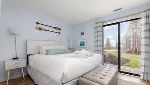 Een slaapkamer met een groot bed, een nachtkastje, een lamp en uitzicht op de omgeving.