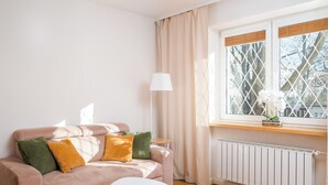 A cozy living room with a pink sofa, a small white side table, and a window with a view of trees.
