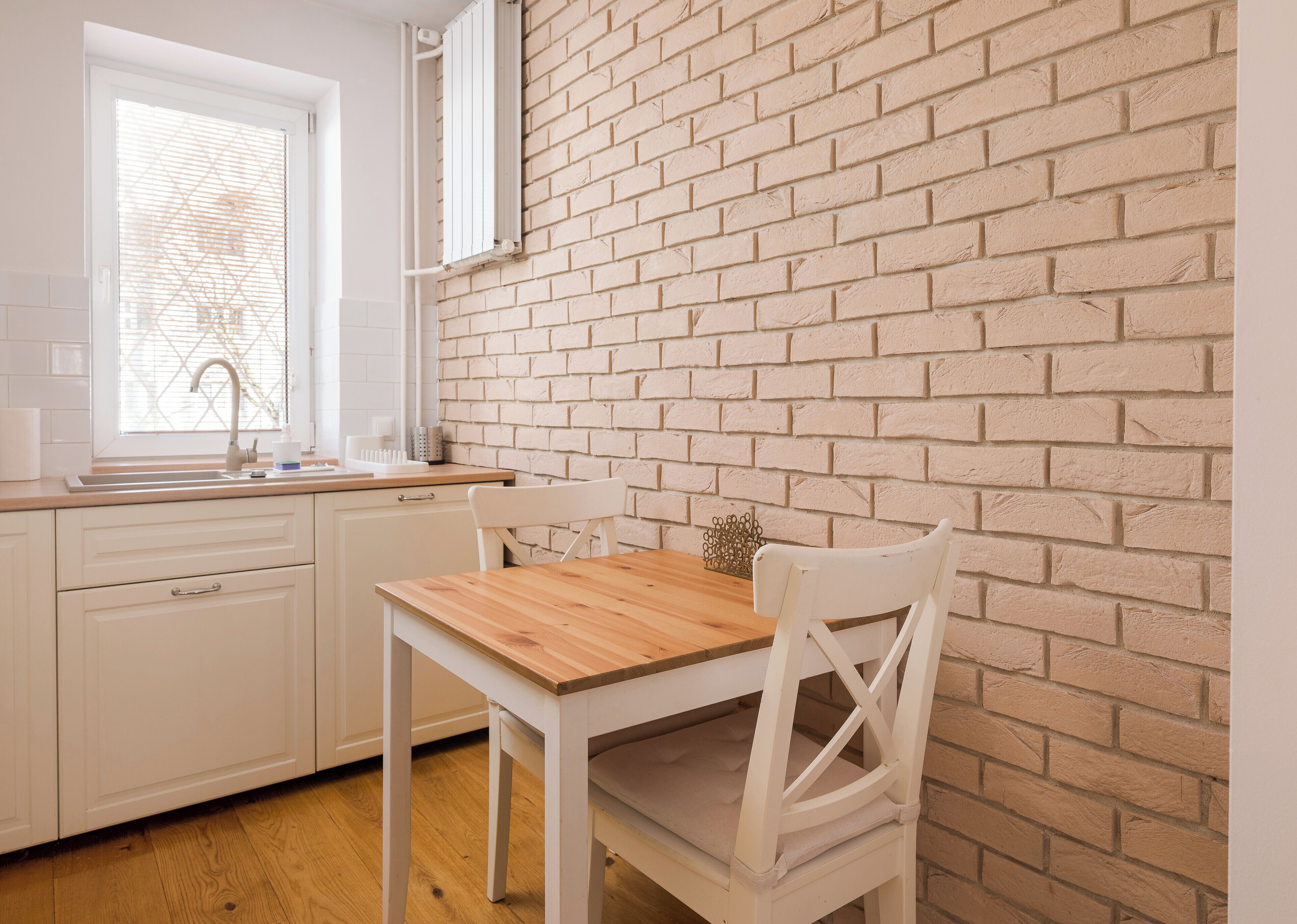 Une cuisine avec des meubles blancs, une table en bois et un mur en briques.