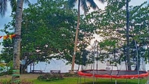 A trampoline in a grassy area with trees and a body of water in the background. - RedDoorz @ St Anthony Beach Resort (Asturias)