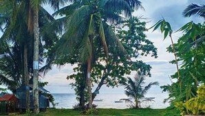 A tropical garden with palm trees and a view of the ocean. - RedDoorz @ St Anthony Beach Resort (Asturias)