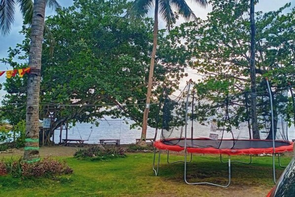 A trampoline in a grassy area with trees and a body of water in the background. - RedDoorz @ St Anthony Beach Resort (Asturias)
