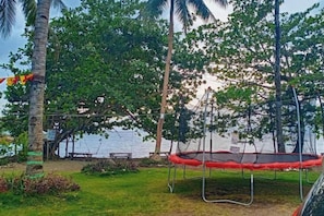 A trampoline in a grassy area with trees and a body of water in the background. - RedDoorz @ St Anthony Beach Resort (Asturias)
