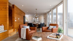 A modern living room with a wooden accent wall, leather sofas, a dining area, and large windows.