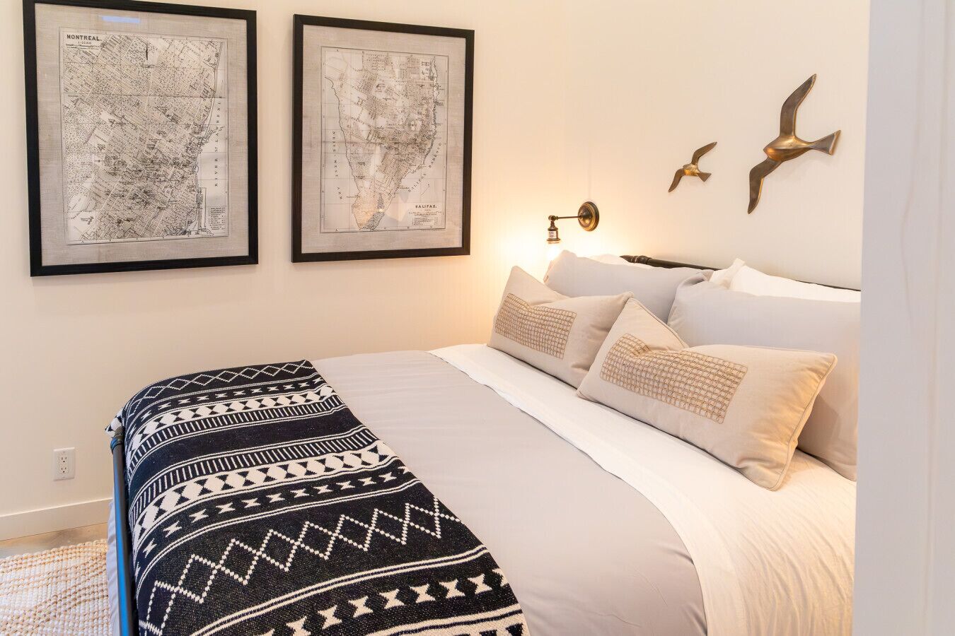 Un dormitorio ordenado con cama, almohadas y dos mapas enmarcados en la pared.