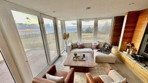A modern living room with a large glass door leading to a patio, a wooden fireplace, and a cozy seating area.