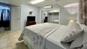 A bedroom with a bed, a TV, a wardrobe, and a window with curtains. - Bamboo – New Apt. - Downtown/Sea View - Perfect Location (Charlotte Amalie West)