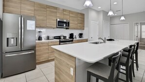 A modern kitchen with stainless steel appliances, wooden cabinets, a central island with bar stools, and pendant lighting. - 163KB - Balmoral Resort, a spacious 4-bedroom retreat perfect for families (Haines City)