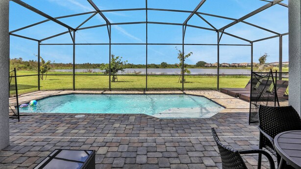 Un espacio al aire libre cubierto con piscina, mobiliario de patio y vistas a un campo de césped y edificios lejanos.