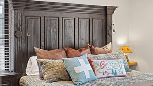A bed with a quilted bedspread and multiple pillows, a dark wooden headboard, and a bedside table with a lamp.