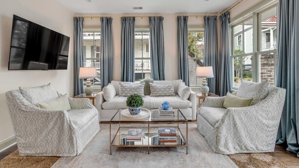 A spacious living room with a large flat-screen TV, two patterned armchairs, a central sofa, and a coffee table with books and decorative items. - The Manor 93 A&B - 2 Newly Renovated Units in Downtown Charleston! (Charleston)