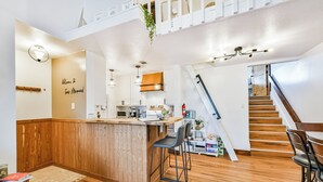 A modern kitchen with a wooden island, bar stools, and a staircase leading to an upper level.