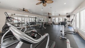 A gym with treadmills, weight machines, and ceiling fans.