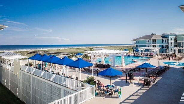 A resort pool area with umbrellas, lounge chairs, and a view of the beach.