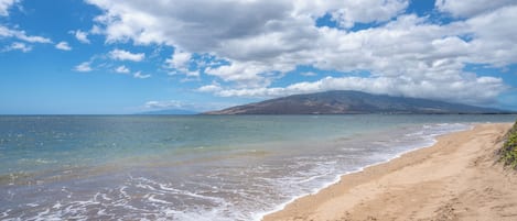 Di pantai, pasir putih, kursi berjemur, dan payung pantai