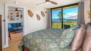 A bedroom with a large bed, a ceiling fan, and a view of the ocean. - Hip Hawaiian Seaside Vistas (Kihei)