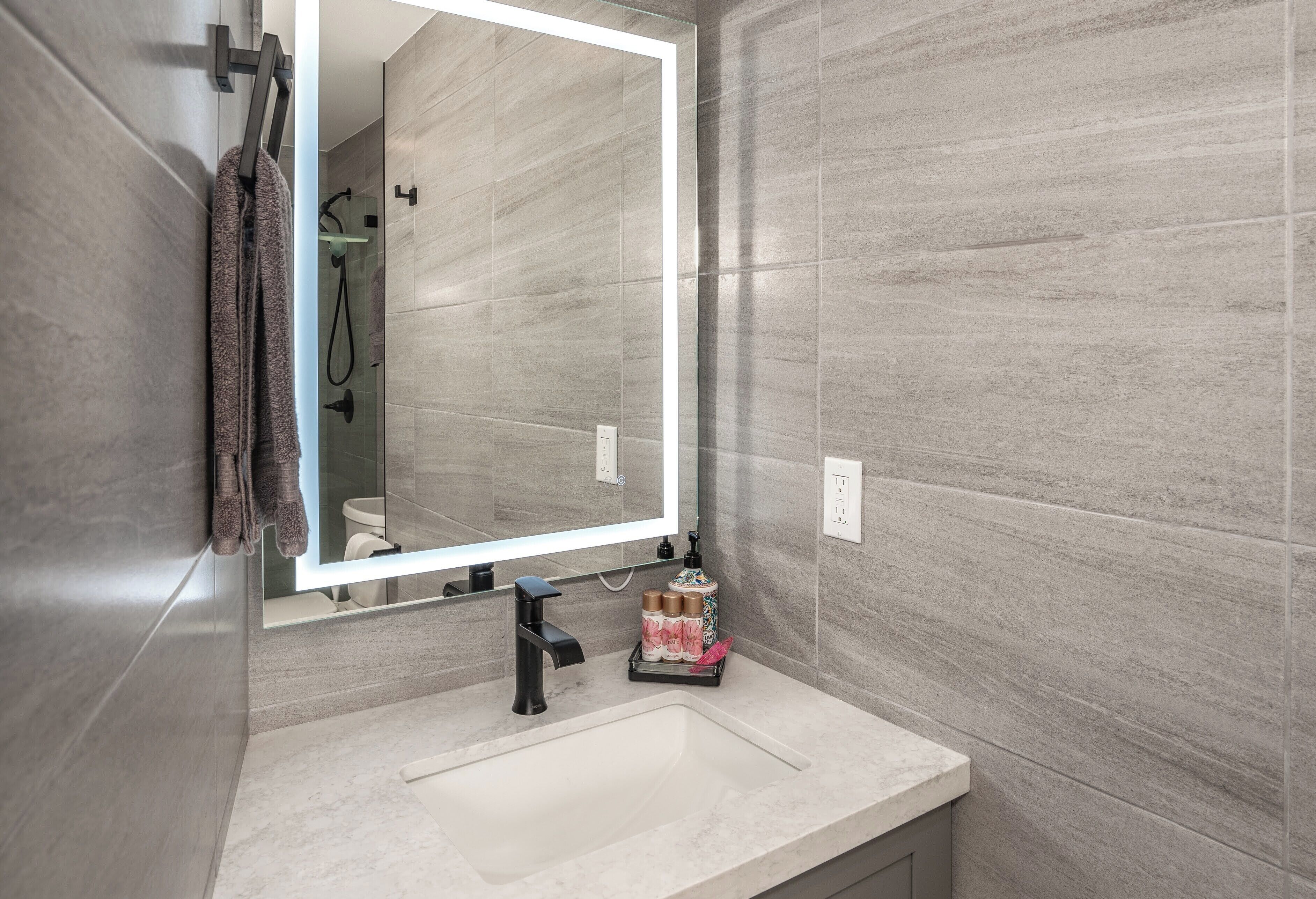 A modern bathroom with a large mirror, a sink, and a towel rack.