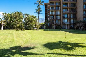 A well-maintained lawn with a flag marker, surrounded by palm trees and a multi-story building with balconies. - Hip Hawaiian Seaside Vistas (Kihei)