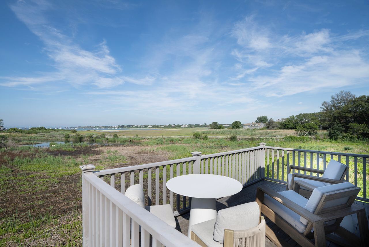 A deck with a round table and two sofas, overlooking a grassy field and a body of water.