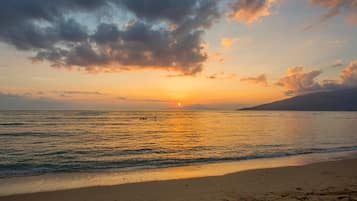 Una spiaggia con impronte che conducono all'acqua, un tramonto sullo sfondo e una montagna in lontananza.