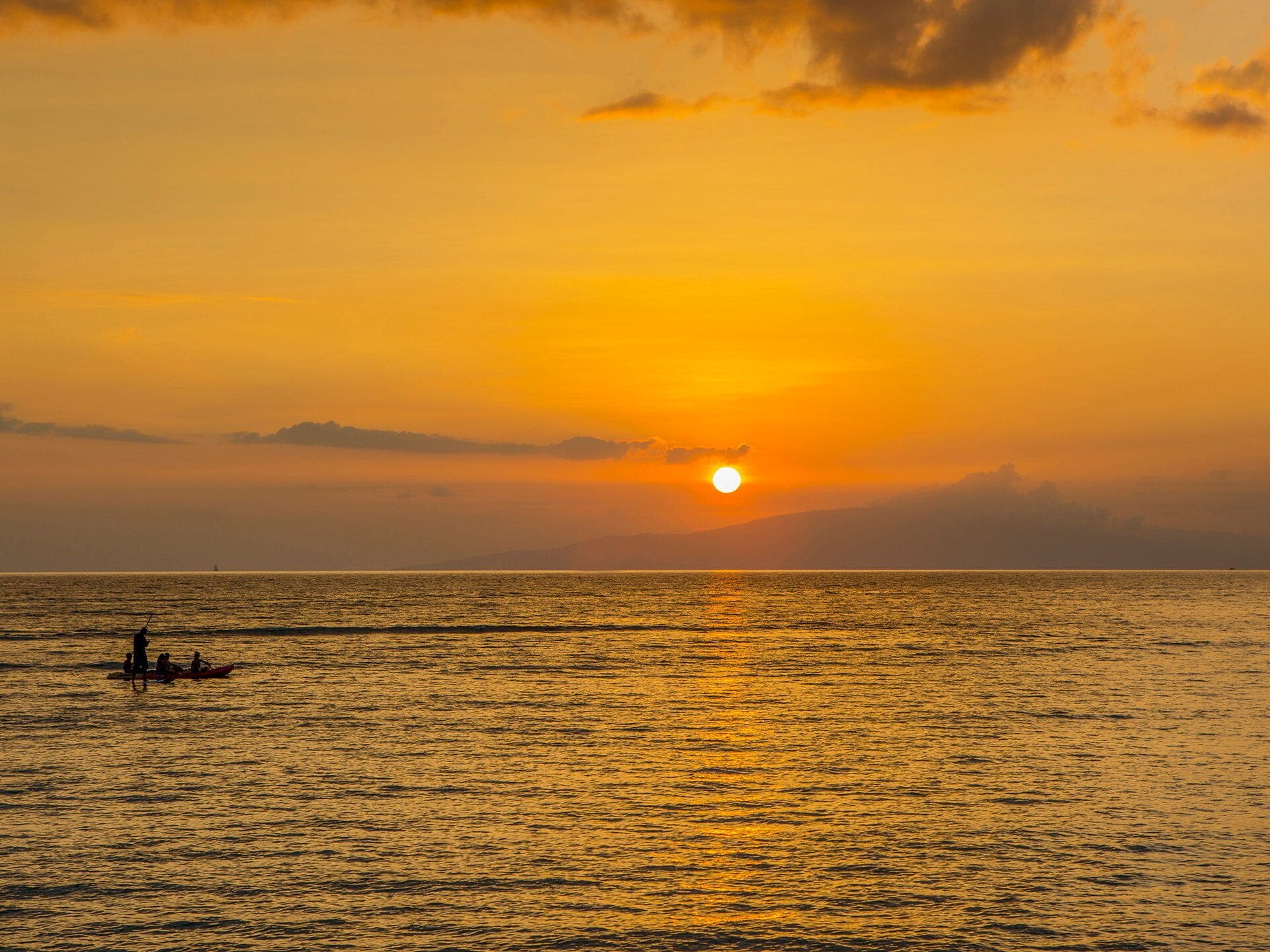 Un coucher de soleil sur une mer calme, avec un petit bateau et des personnes au premier plan.