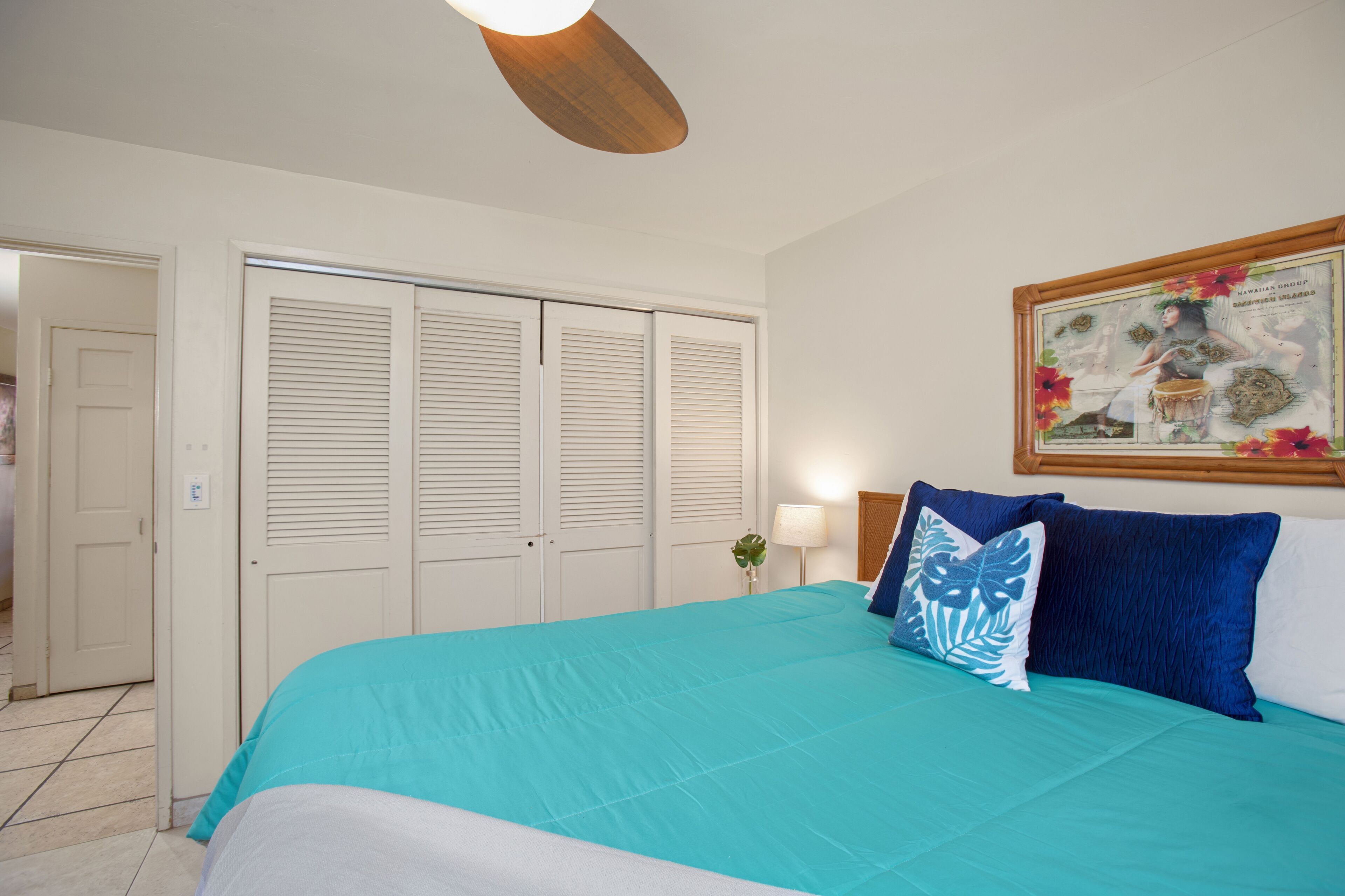 A bedroom with a large bed, white shutters, a framed picture on the wall, and a ceiling light fixture.