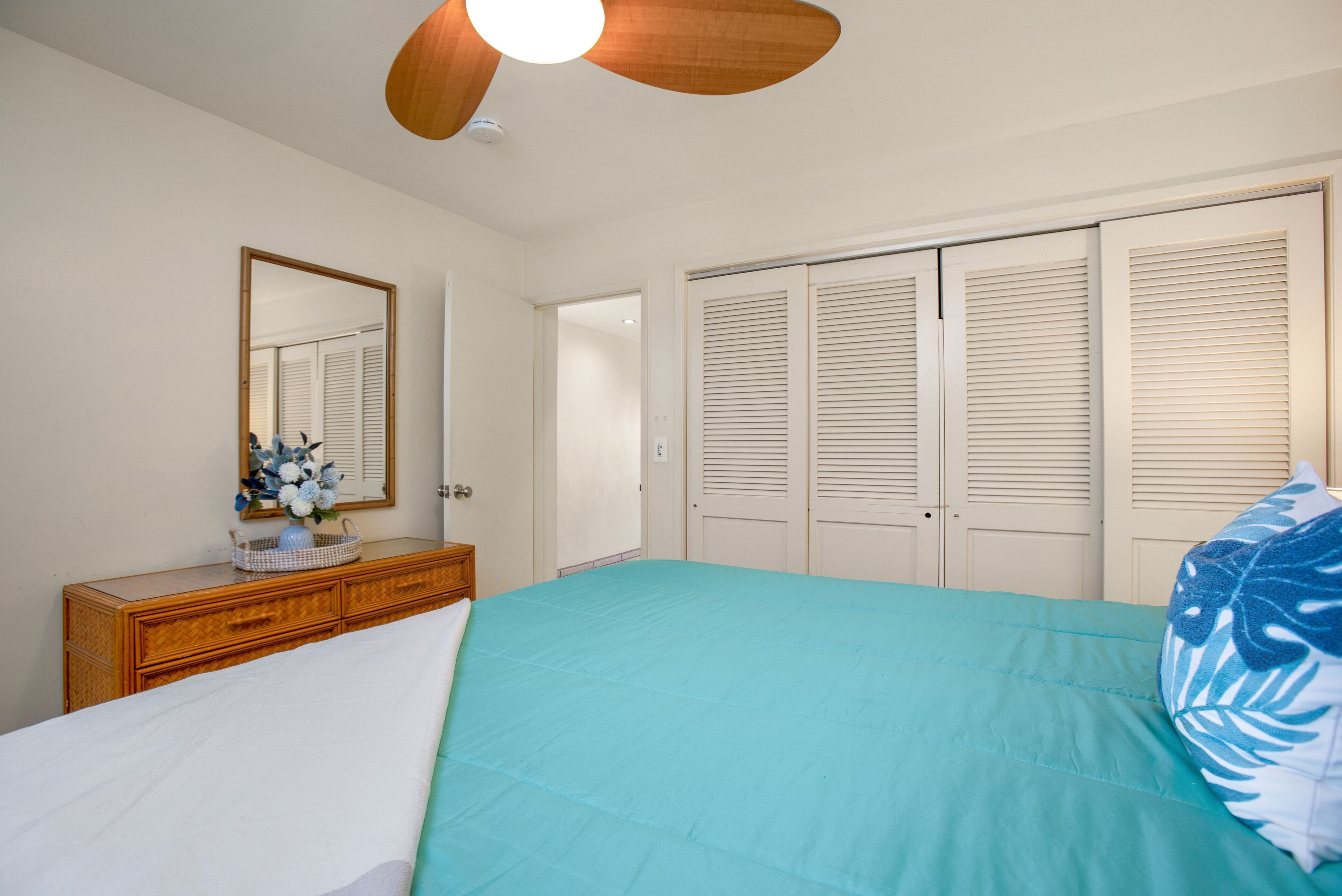 Un dormitorio con cama, cómoda, espejo y armario con puertas operculadas.