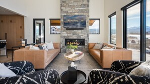 Una sala de estar moderna con chimenea de piedra, sofás de cuero y ventanas amplias con vistas al exterior.